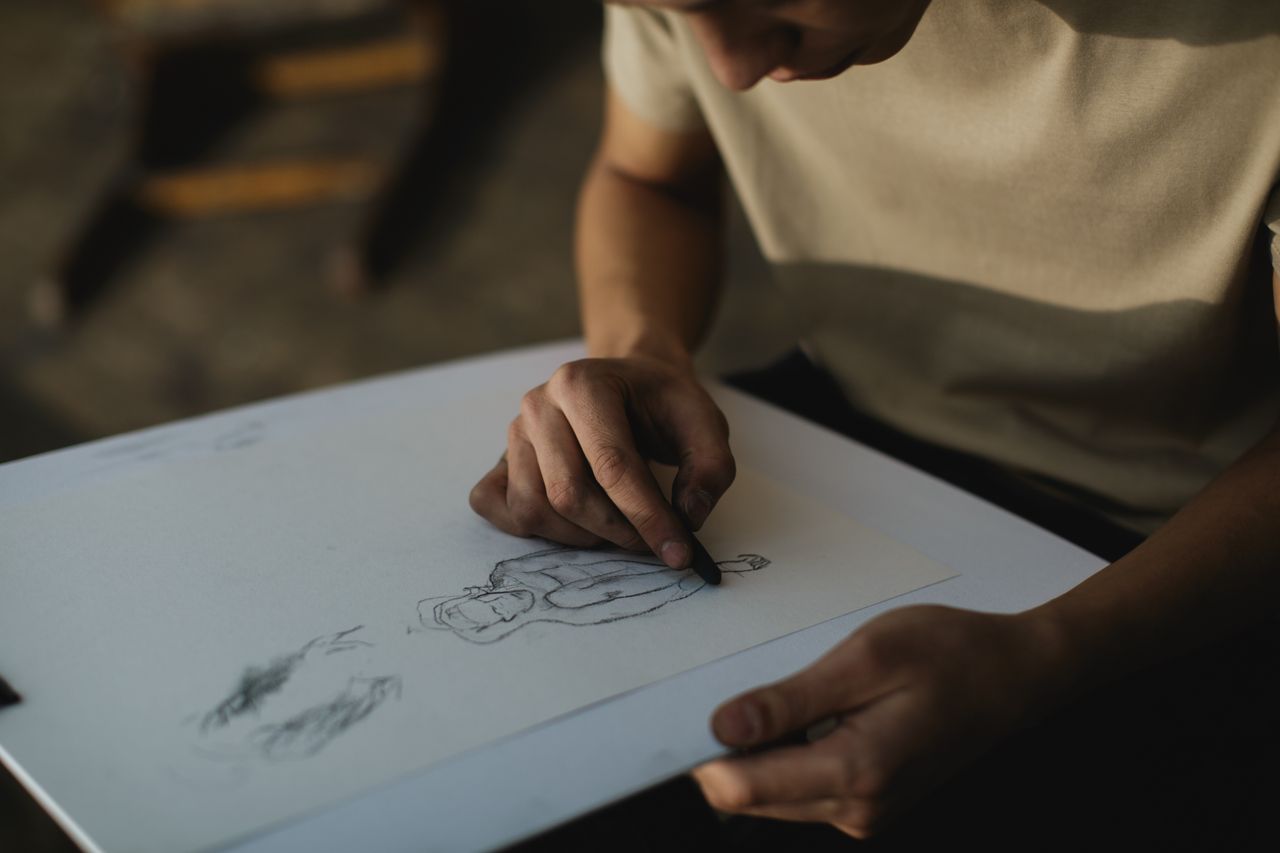 close up of a person sketching on paper with concentrated focus indoor