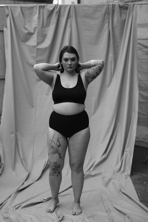 Free Black and white portrait of a tattooed woman standing confidently in swimwear with a serious expression. Stock Photo