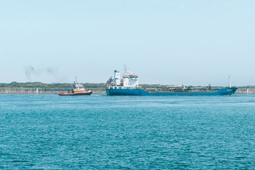 Free A cargo ship and tugboat sail on a clear, sunny day across the blue ocean. Stock Photo