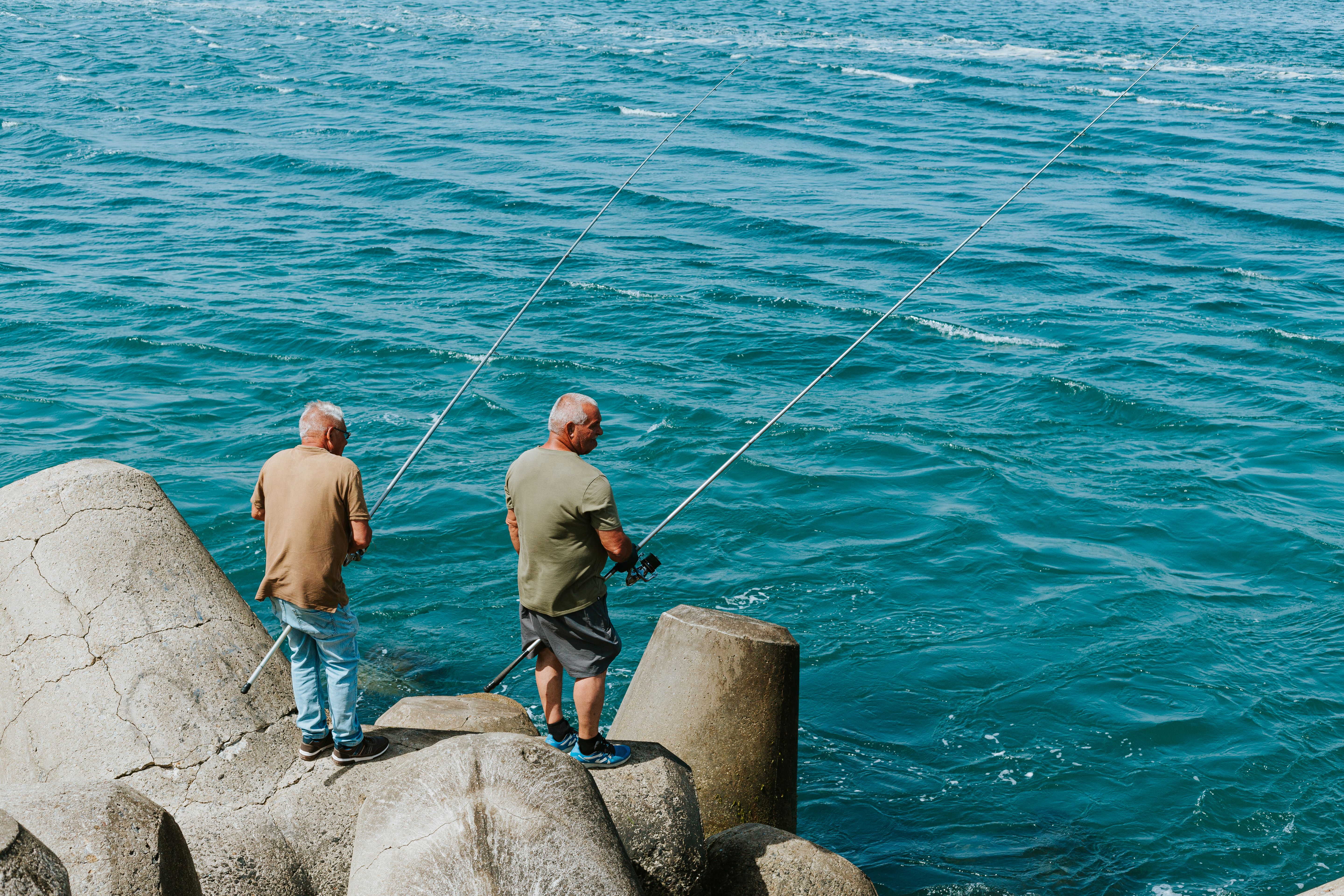 Two senior men fishing on a concrete seawall by the ocean on a sunny day.