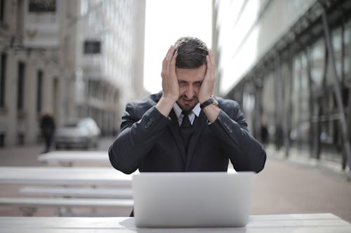 Man in Black Suit Covering His Face With Two Hands