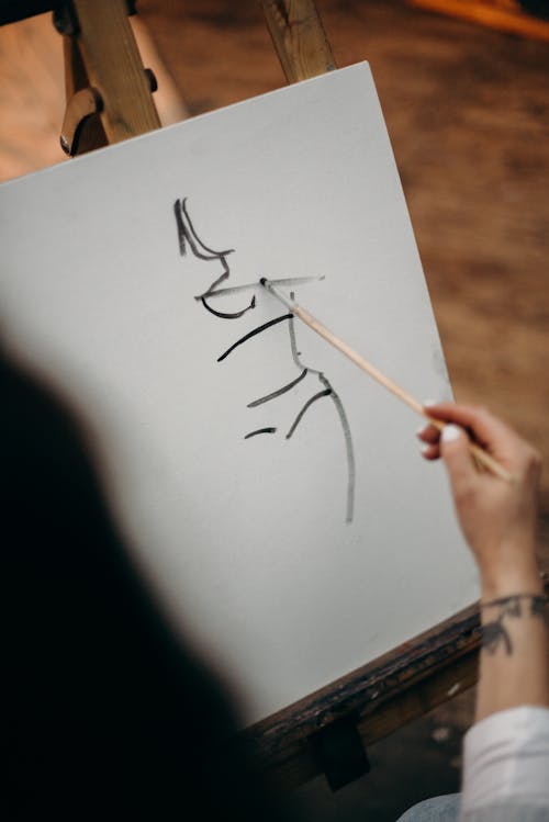 Person Holding Wooden Brush Drawing on White Canvas