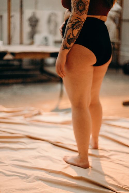 Free Artistic nude woman standing in a studio environment, showcasing body tattoos and confidence. Stock Photo
