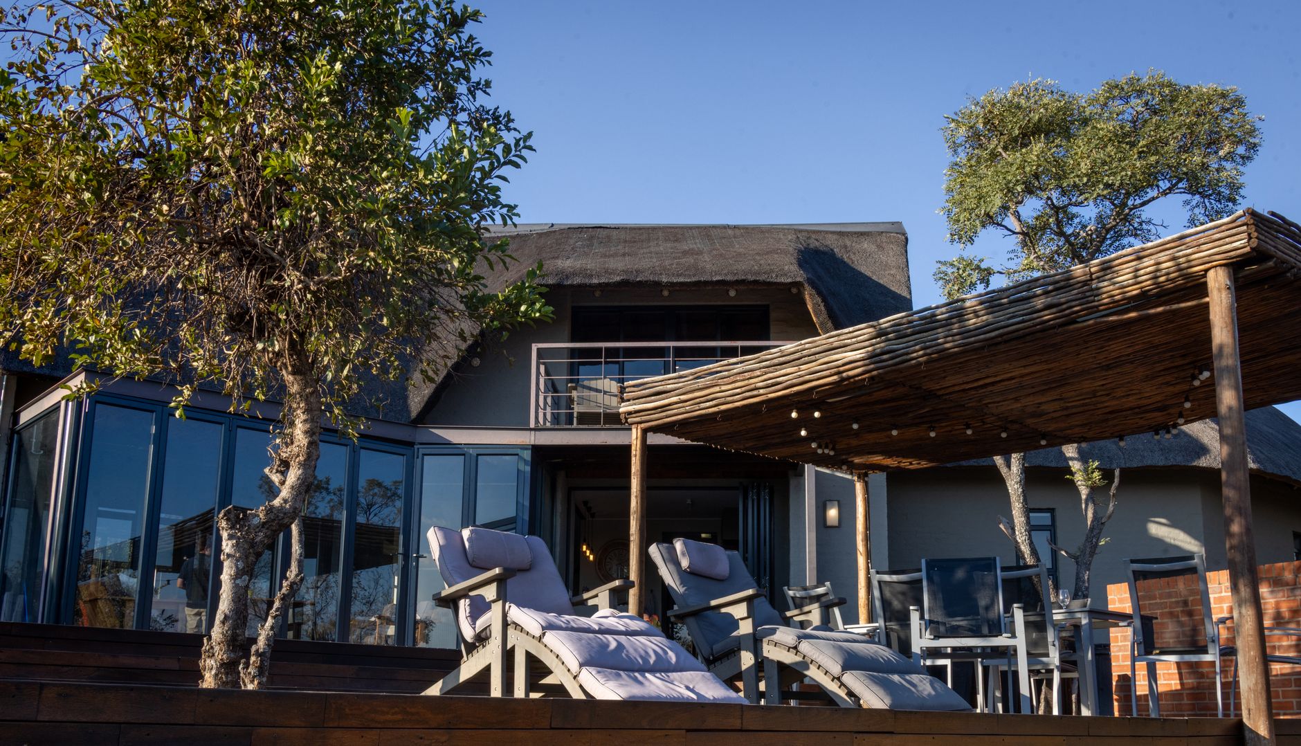 Elegant outdoor patio at a modern safari lodge with sun loungers and natural wood pergola.