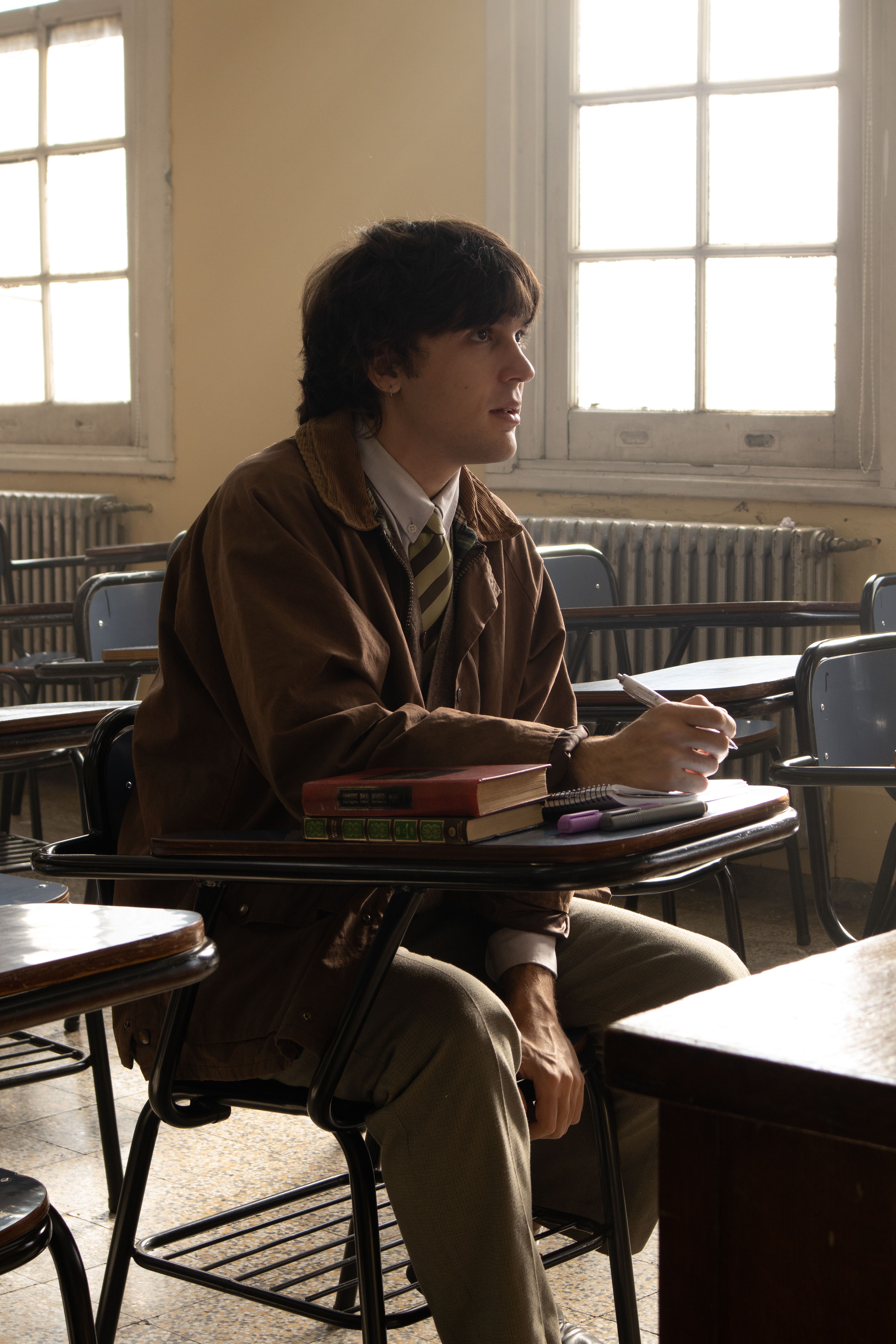 A thoughtful student sits in a classroom, surrounded by books and taking notes.