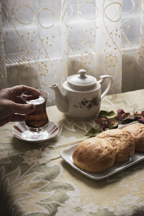 Free A warm afternoon tea setup with fresh bread, a teapot, and a hand holding a cup of tea. Stock Photo