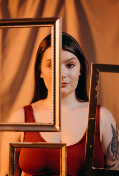 Free Creative portrait of a woman posing with empty frames in a warm-toned studio setting. Stock Photo