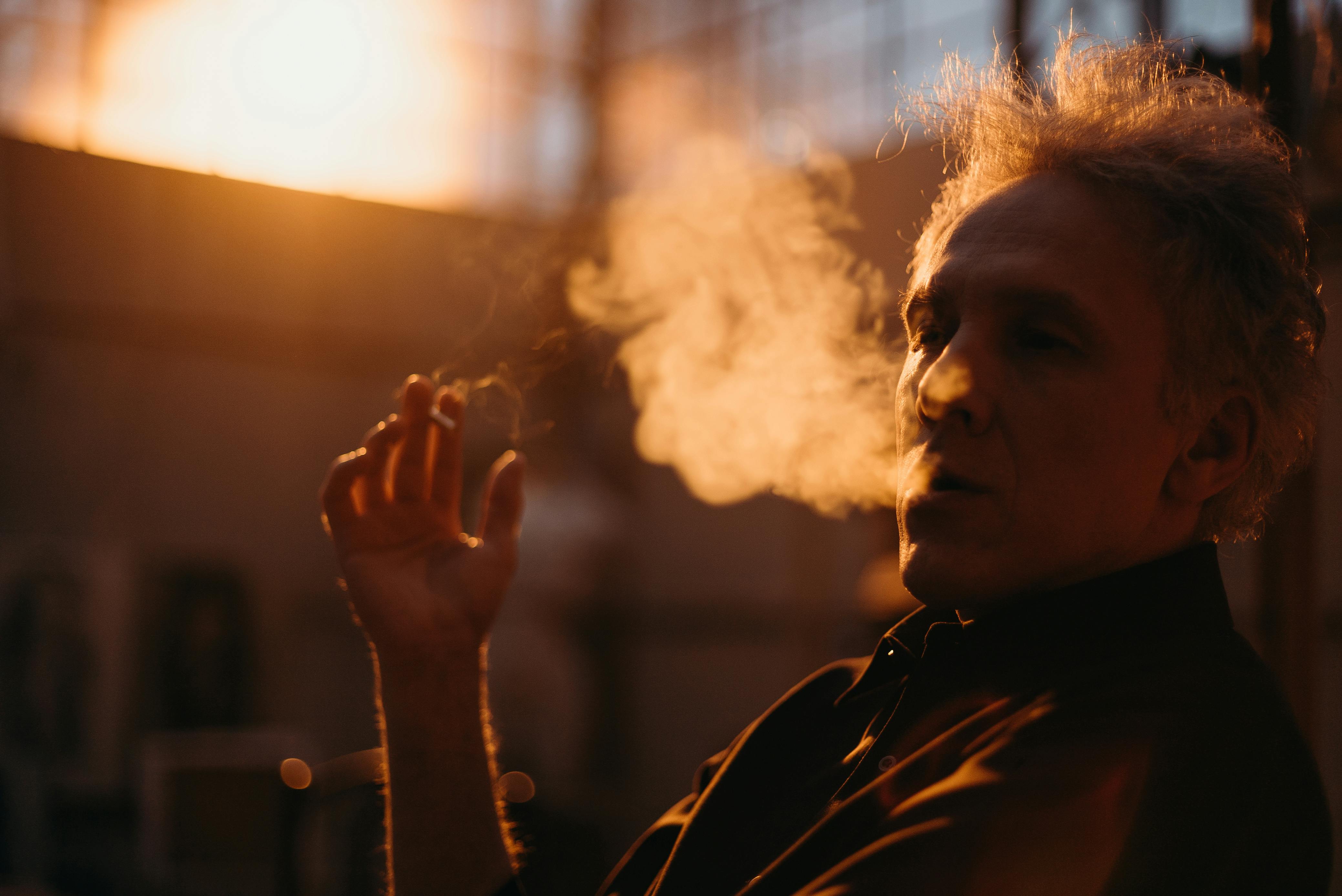 一名男子在室内吸烟，在日出或日落的灯光下，烟雾被清晰地映照出来