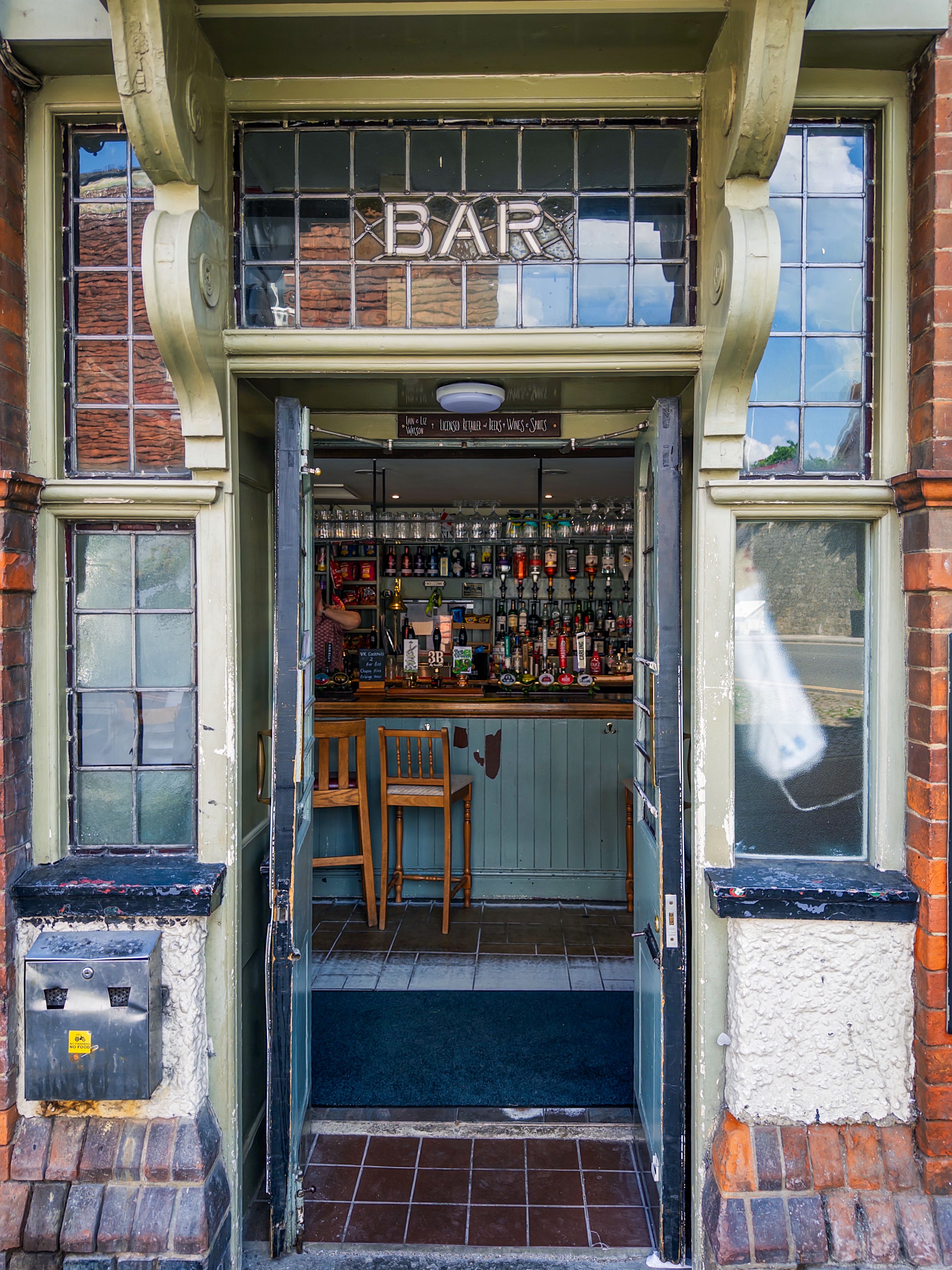 A welcoming entrance to a traditional English pub with a well-stocked bar inside.
