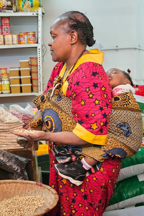 Free African woman in red traditional attire shopping with baby on her back in Johannesburg market. Stock Photo