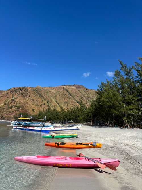 Free Vibrant kayaks on a sunny beach with lush hills, ideal for adventure travel. Stock Photo