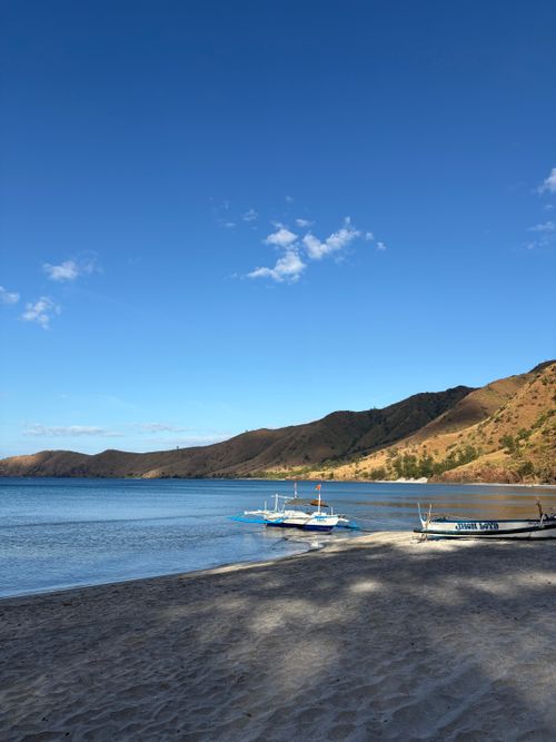Free Scenic view of a tranquil beach with boats and mountains in Zambales, Philippines, under a clear blue sky. Stock Photo