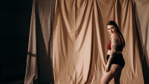 Free Confident plus-size woman with arm tattoo posing in a studio setting, smiling. Stock Photo