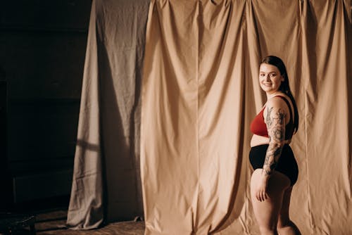 Woman in Red Brassiere Standing Near Brown Curtain