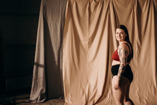 Free Smiling woman in lingerie with tattoo posing confidently indoors. Empowerment and body positivity theme. Stock Photo