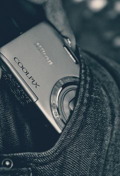 Close-up of a compact camera partially tucked into a denim pocket, featuring a stylish monochrome look.