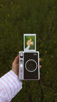 A hand holds an instant camera capturing a vibrant flower photo in a lush green outdoor setting in Türkiye.