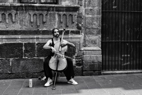Free Black and white photo of a street cellist playing in an urban setting against a stone wall. Stock Photo