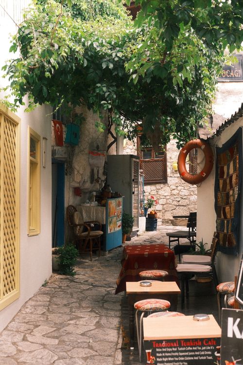 Free A quaint Mediterranean alley featuring a cozy outdoor cafe and lush greenery overhead. Stock Photo
