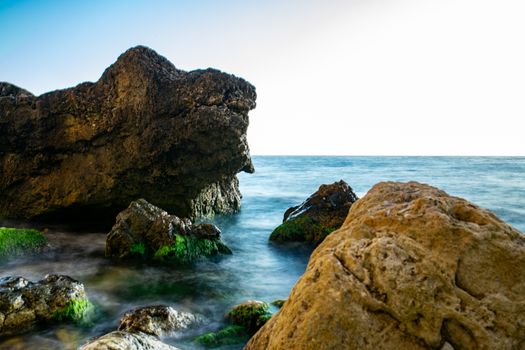 Explore a serene rocky shoreline with algae-covered rocks and clear blue sea at dawn.