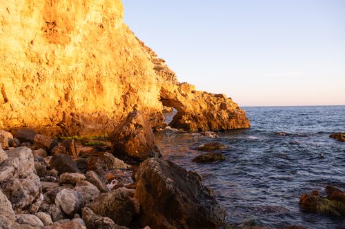 Free Stunning view of sunlit rocky cliffs and ocean waves in a scenic coastal landscape. Stock Photo