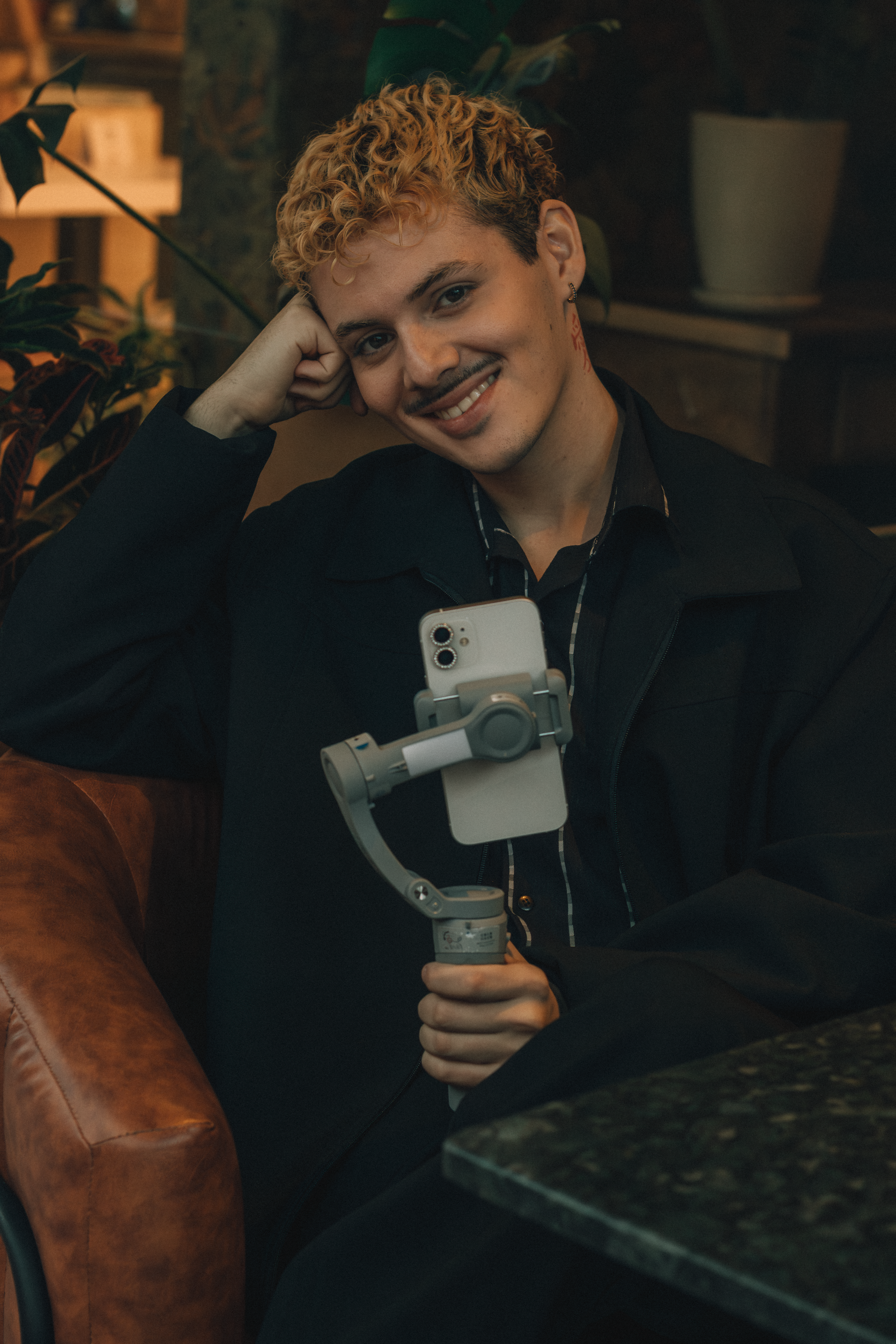 Smiling young adult using smartphone on a gimbal indoors, cozy atmosphere.