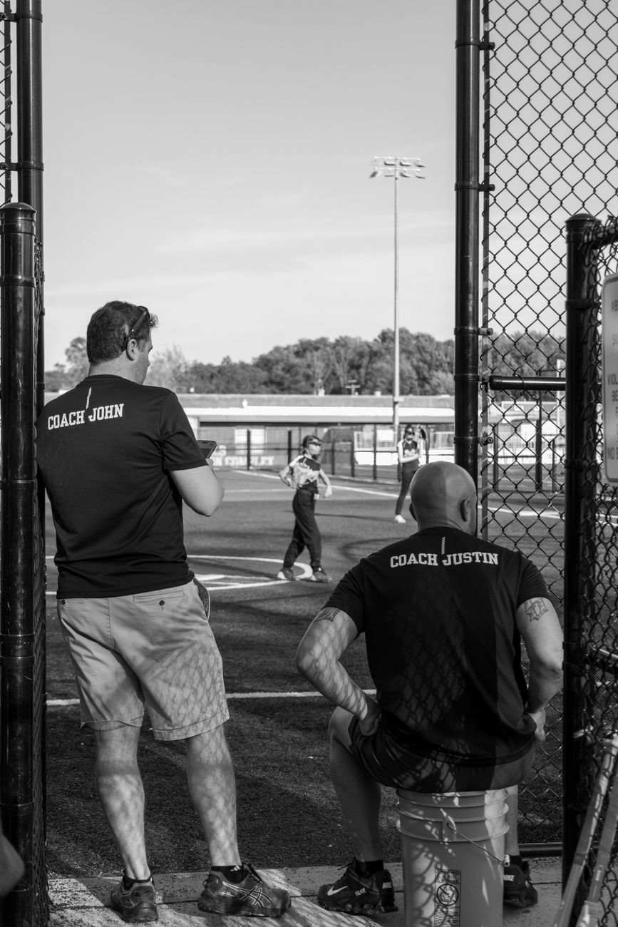 Baseball coaches watching a game at a local park with players on the field.