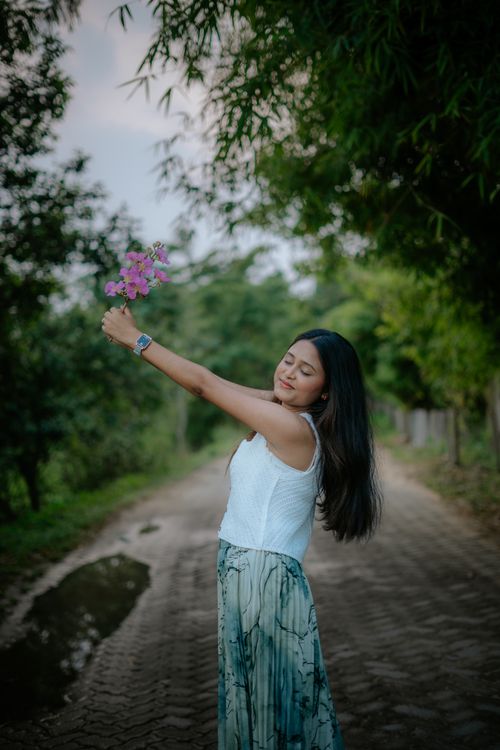 Free A young woman with long hair holding flowers and enjoying nature on a tranquil path. Stock Photo
