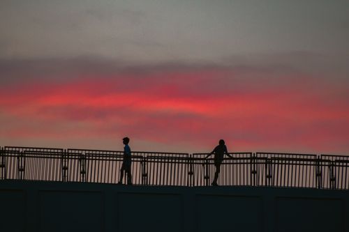 Free Two people silhouetted against a vibrant sunset sky on a bridge in Washington, DC. Stock Photo