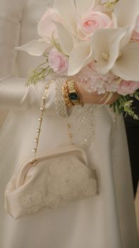Close-up of a bride holding a pastel bouquet, gold jewelry, and an elegant purse.