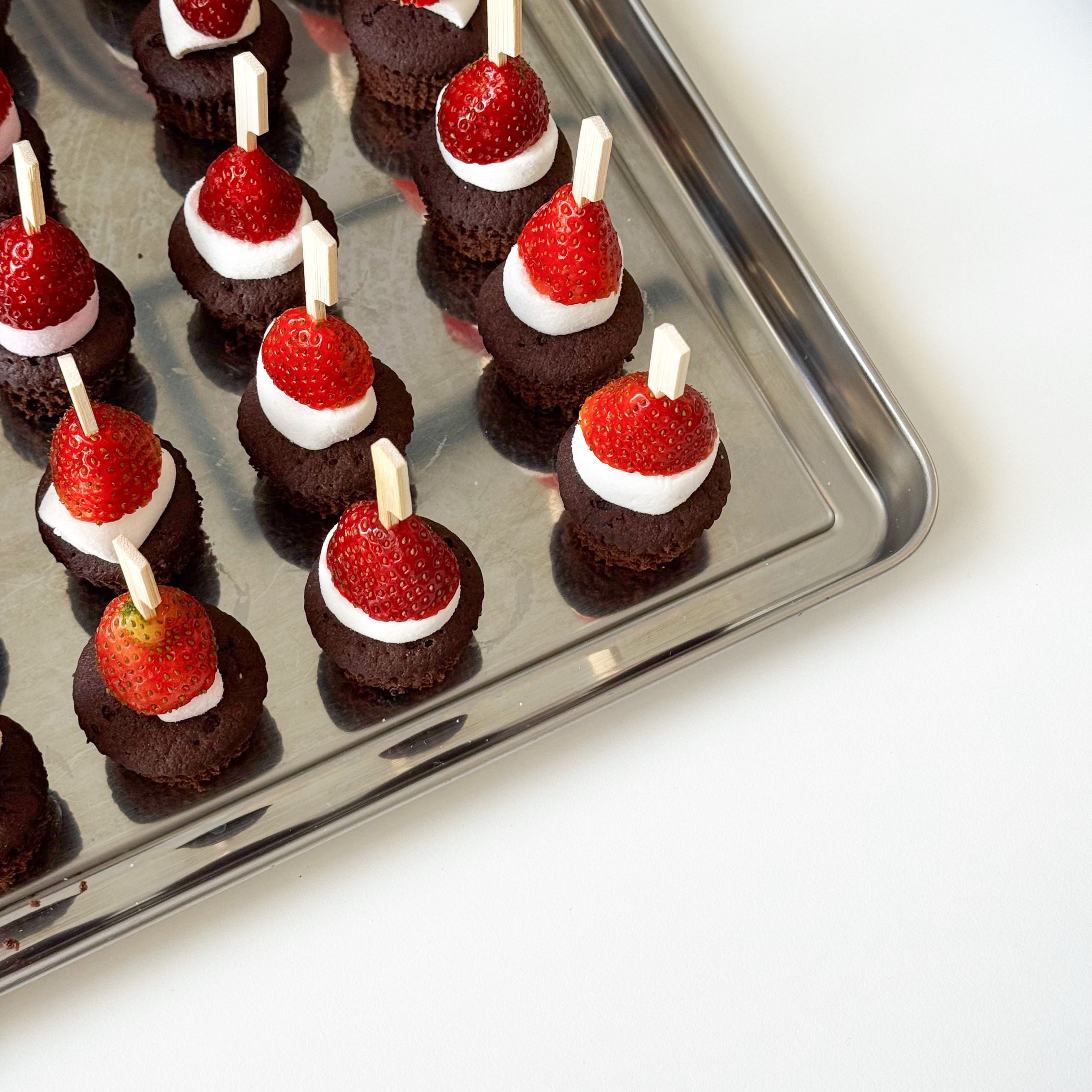 A tray of chocolate muffins topped with strawberries and cream, perfect for dessert.
