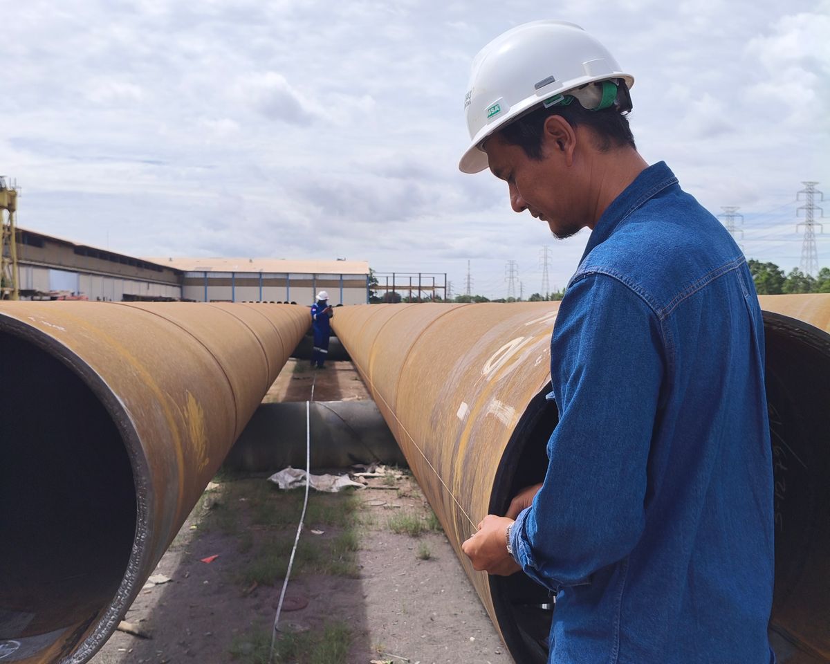 Workers in helmets inspecting large pipes at an outdoor job site.