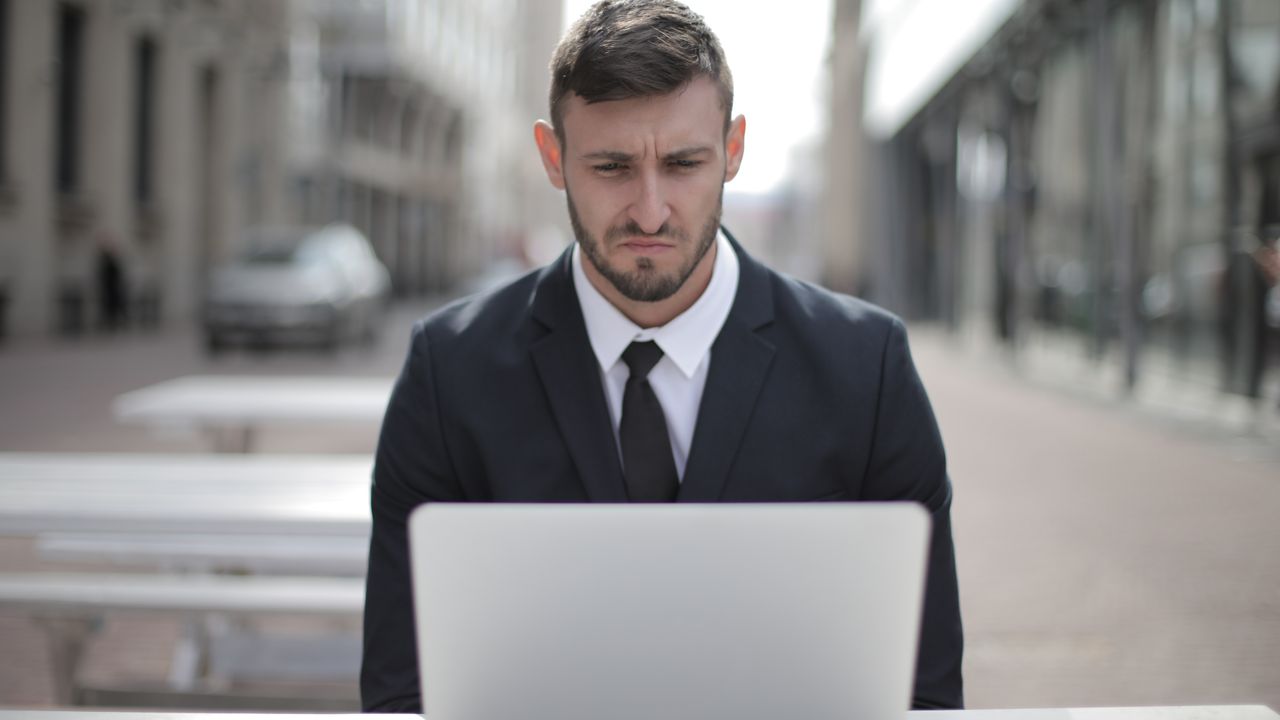 A focused businessman in a suit works on his laptop outdoors in an urban setting.