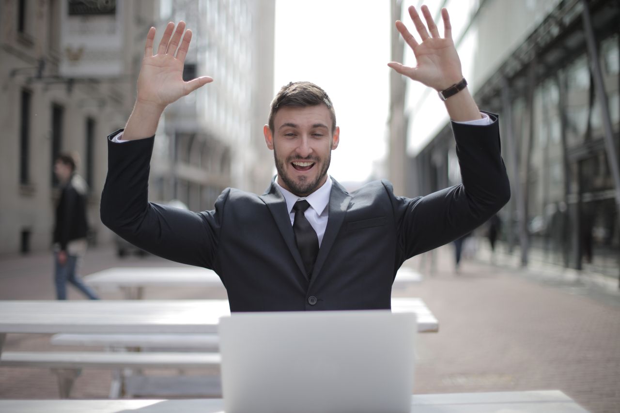 a joyful businessman raises his hands in excitement while working on a