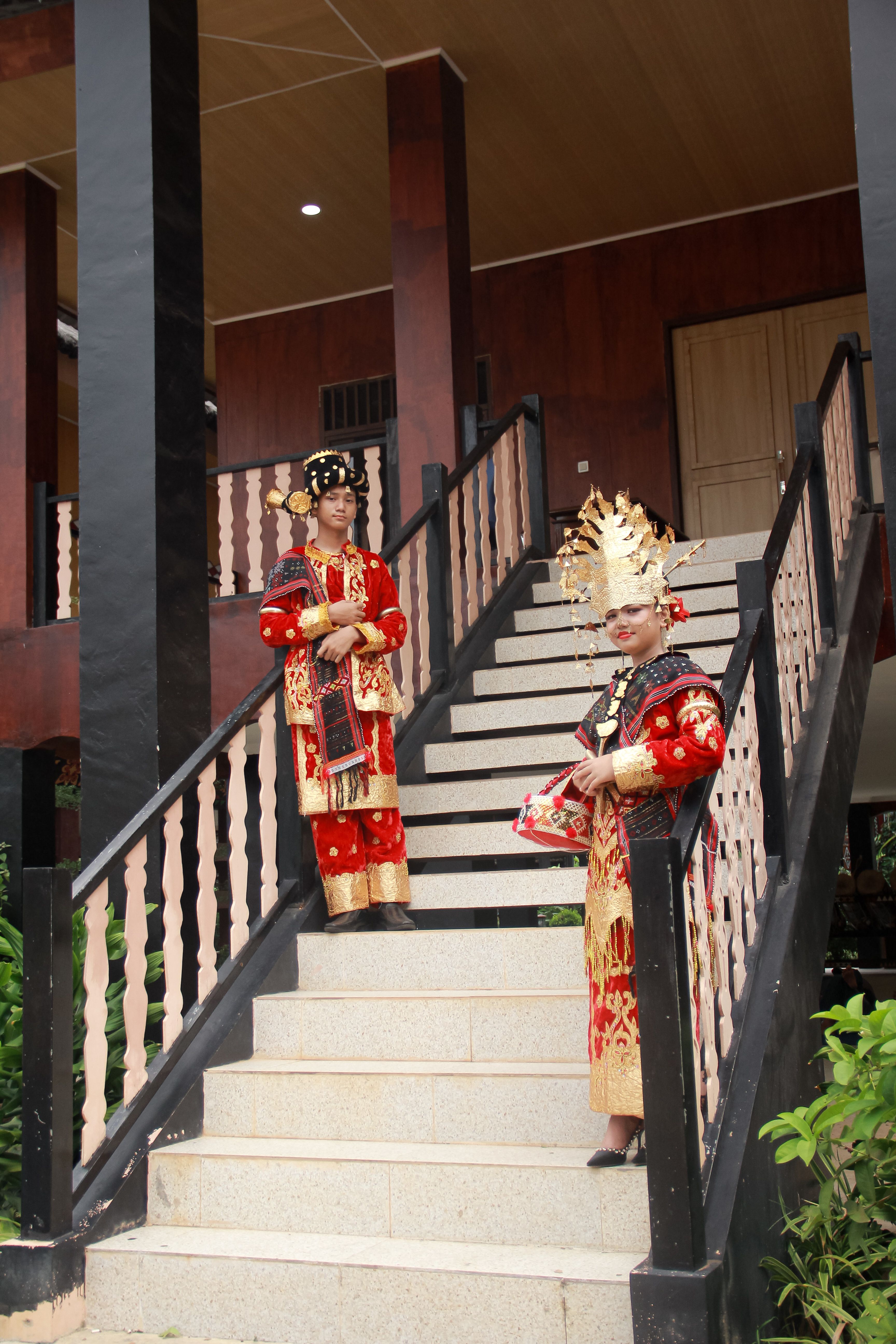 Two individuals in vibrant traditional Indonesian clothing on a staircase outdoors.