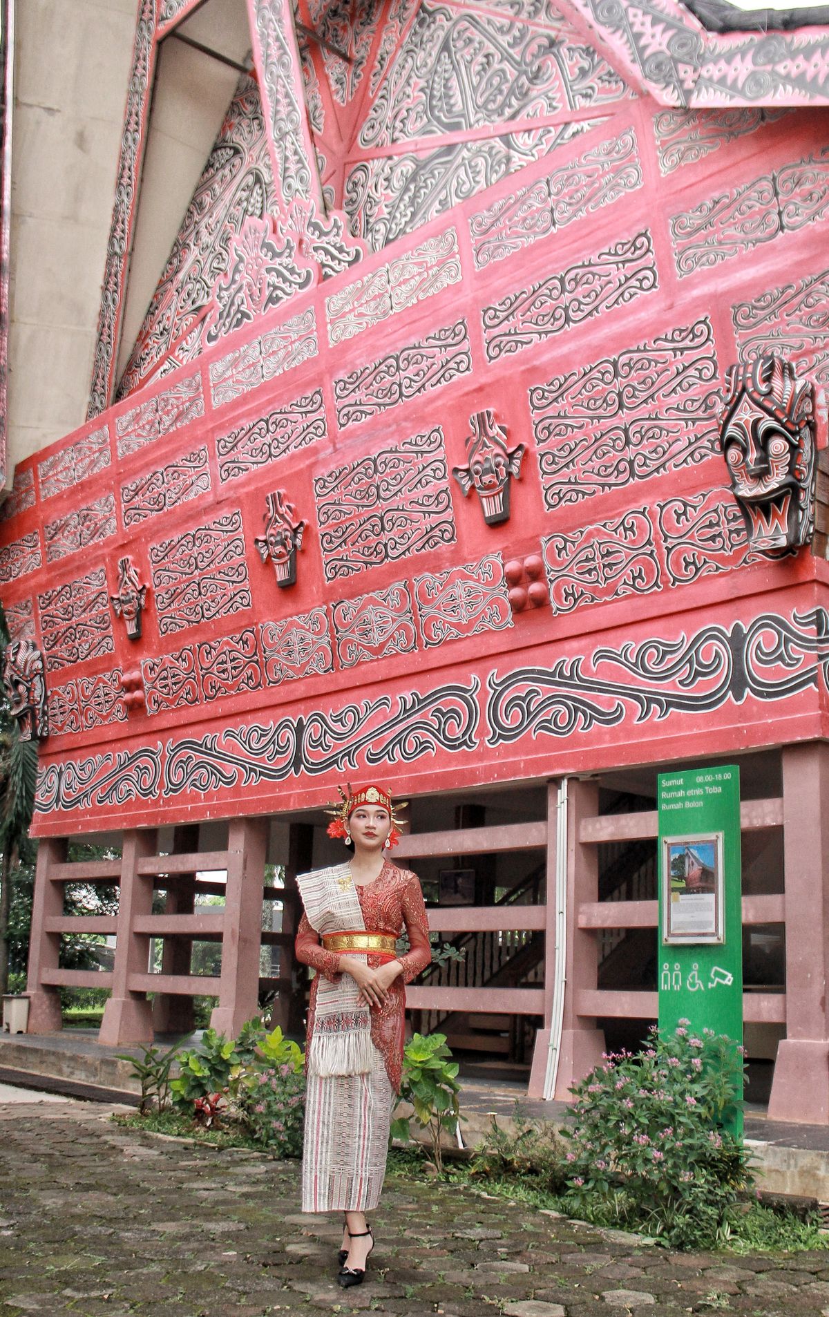 Perempuan mengenakan busana tradisional Batak di depan rumah adat
