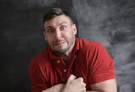 在黑暗背景下，一名身穿红衬衫的男子做出了幽默而夸张的面部表情