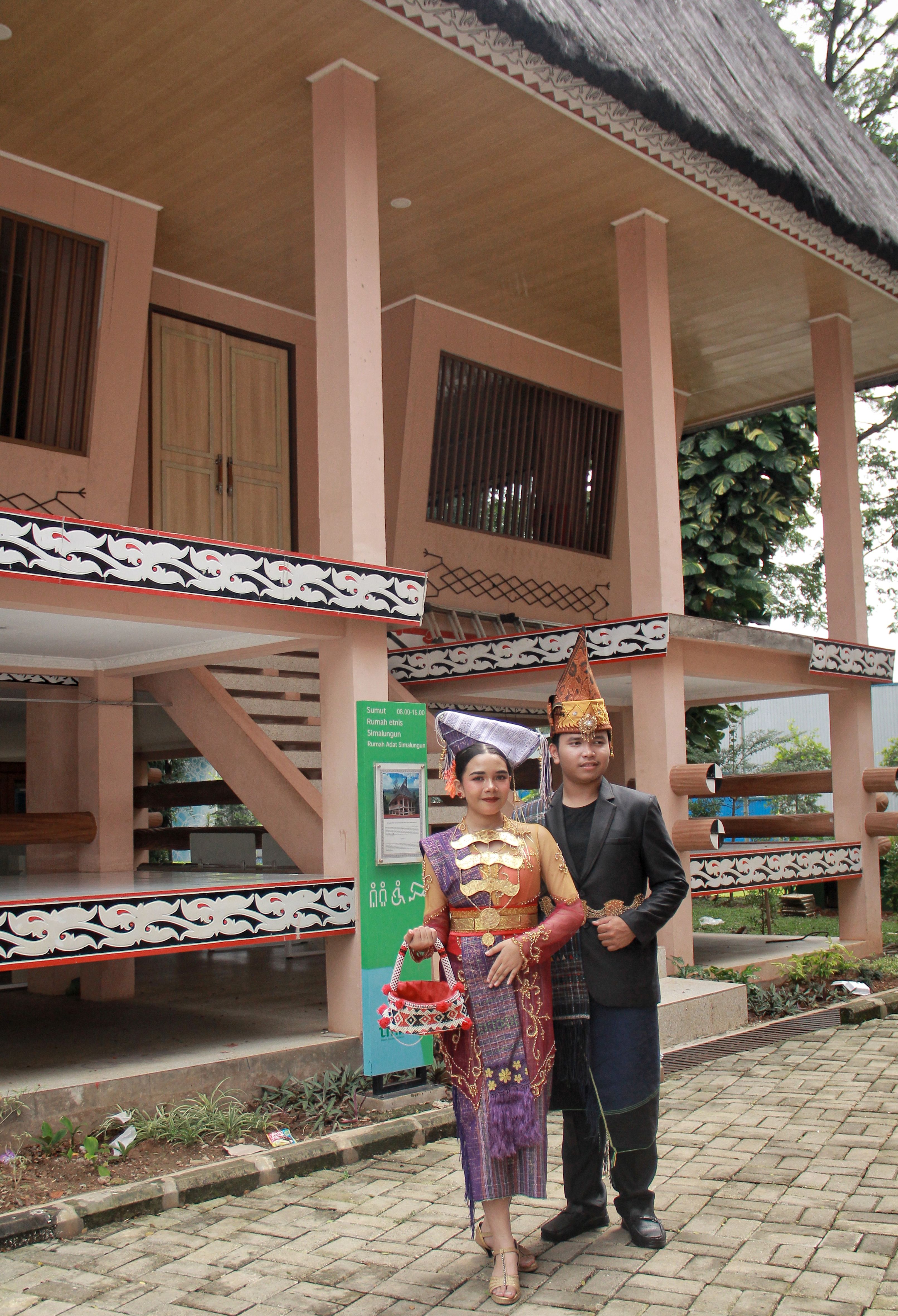 A couple in traditional Indonesian clothing poses near a wooden house in Jakarta, Indonesia.