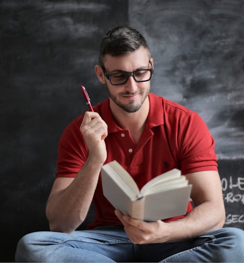 Man in Red Polo Shirt and Blue Denim Jeans Holding Red Pen and Book