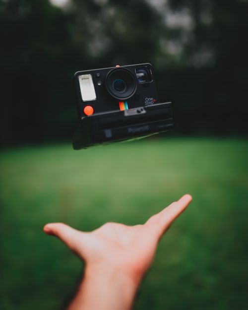 Free A vintage instant camera captured mid-air against a blurred outdoor background. Stock Photo
