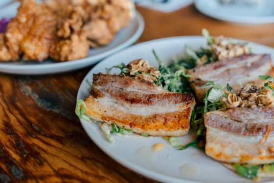 Golden seared pork belly slices over shredded green salad with crispy shallots and nuts