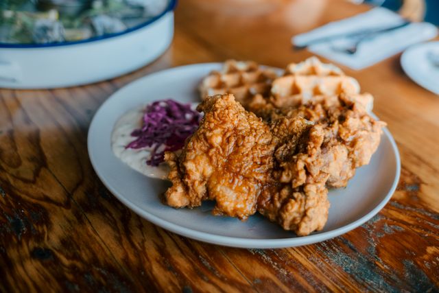 Savory fried chicken with waffles and fresh coleslaw on a rustic table setting.