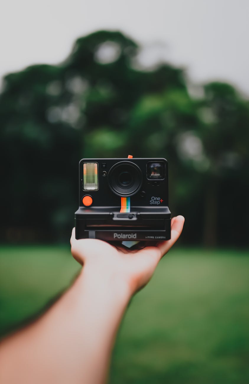 A vintage Polaroid camera held in hand with nature background in Brazil.