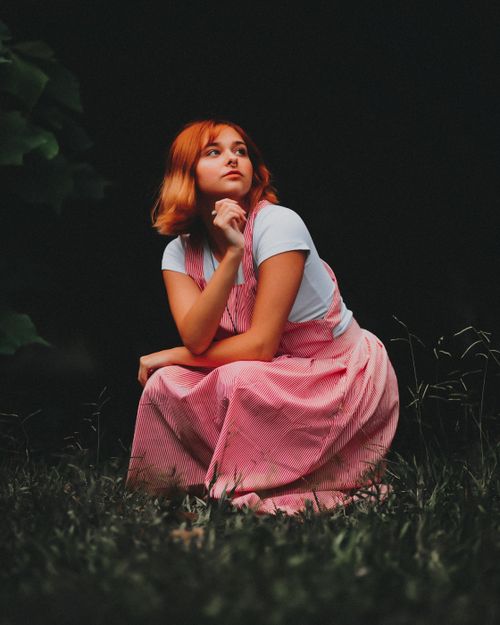 Free A woman in a pink dress sits thoughtfully in a serene outdoor setting. Stock Photo