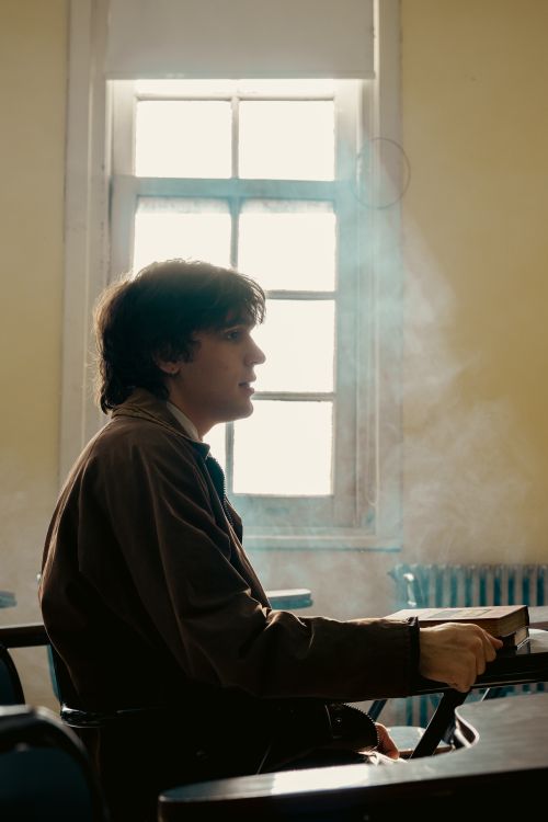 Free A young man sits in a sunlit university classroom, holding a book. Stock Photo