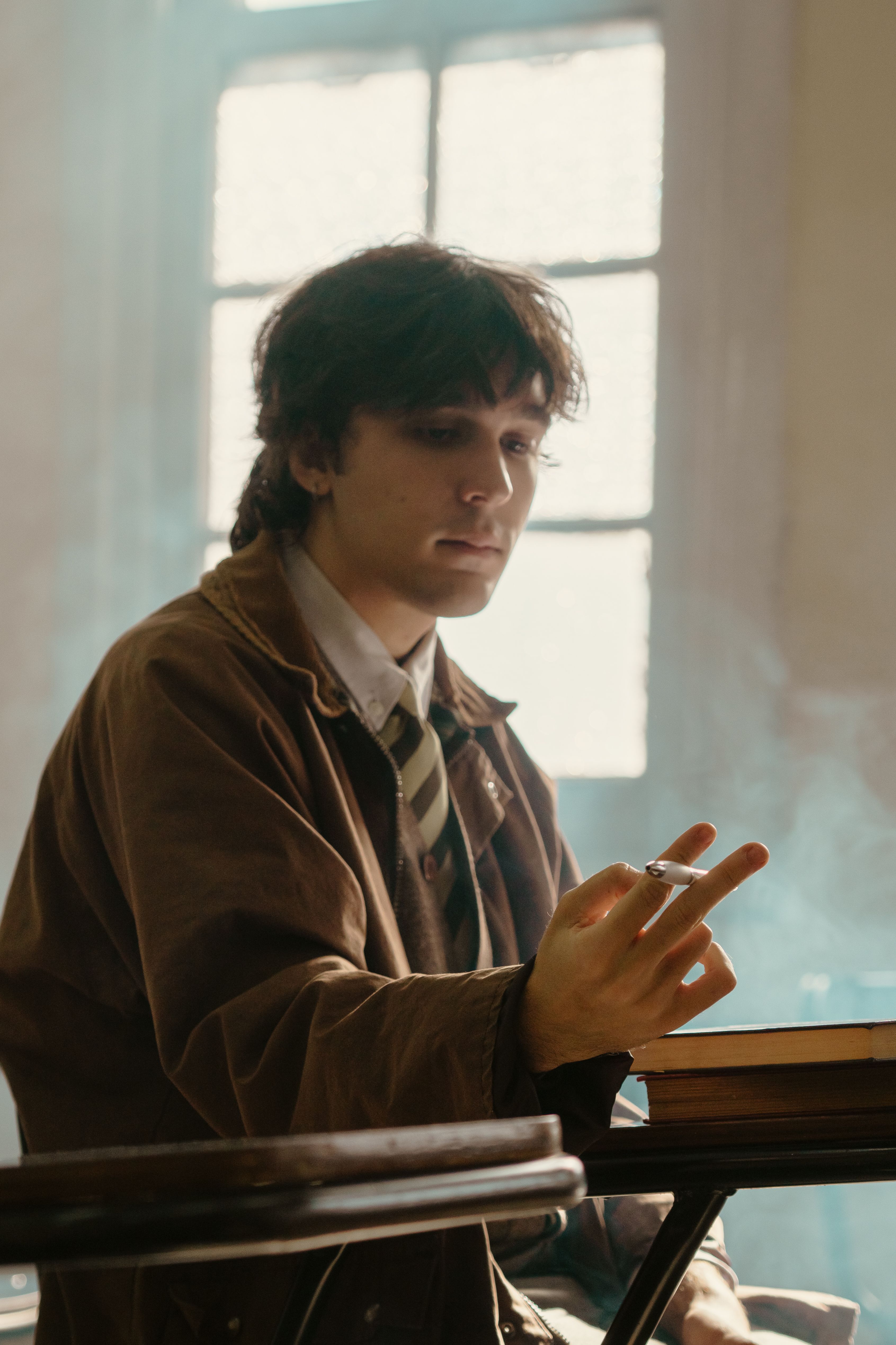 A pensive young man smoking indoors by a window, creating a moody atmosphere.