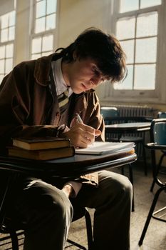 Young male student studying with books in a sunlit classroom, showcasing dedication and focus.