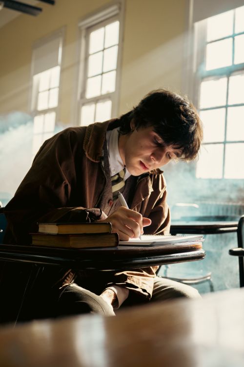 Free A young student concentrates while writing at a desk in a sunlit classroom. Stock Photo