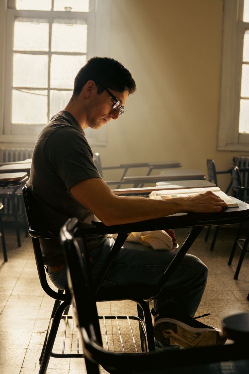 Free Young adult student focused on reading in a sunlit classroom in Buenos Aires. Stock Photo