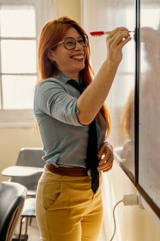 A cheerful teacher engaging with students as she writes on a classroom whiteboard.